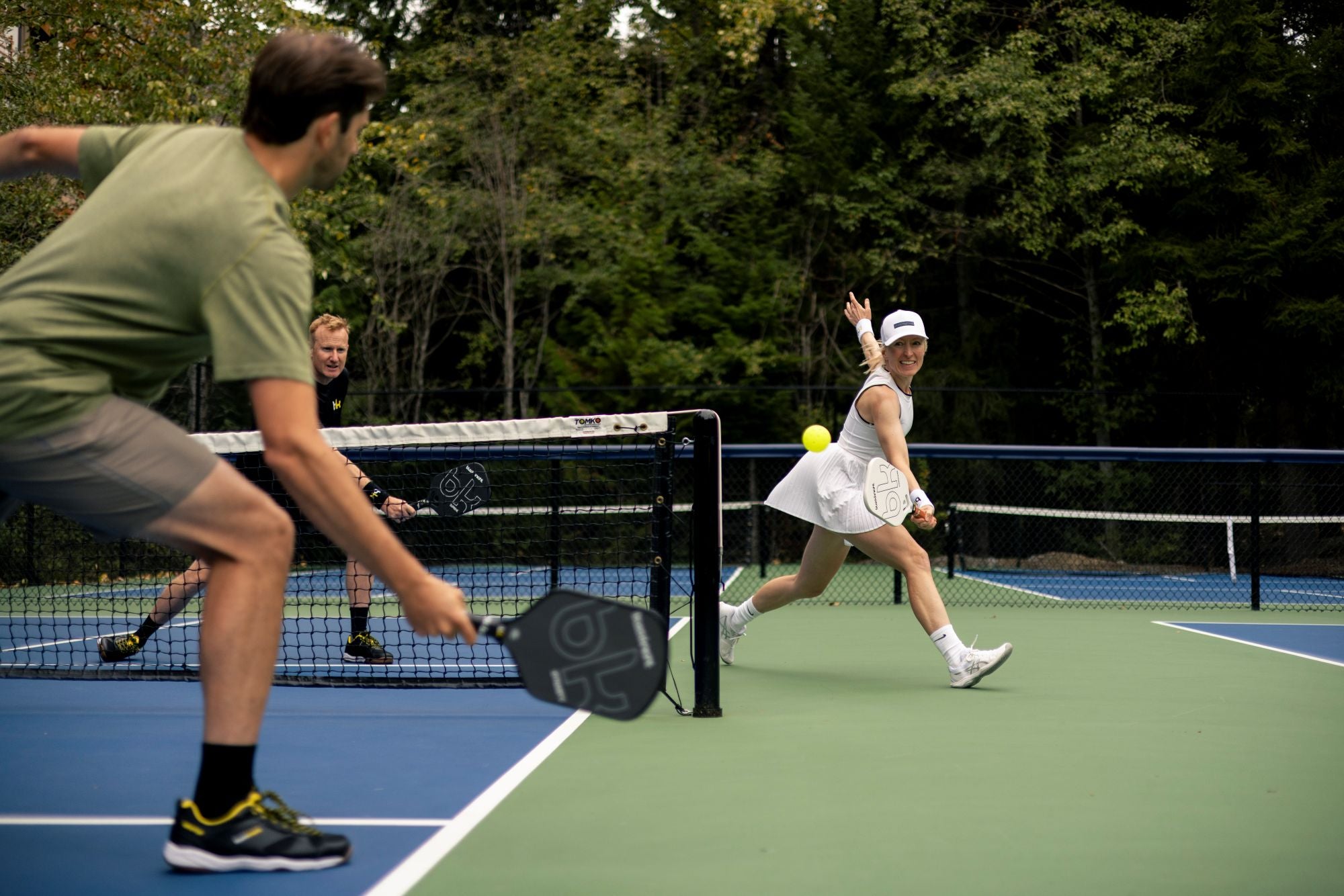Two people playing pickleball on a court with trees in the background