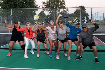 Group of people posing on a pickleball court with paddles
