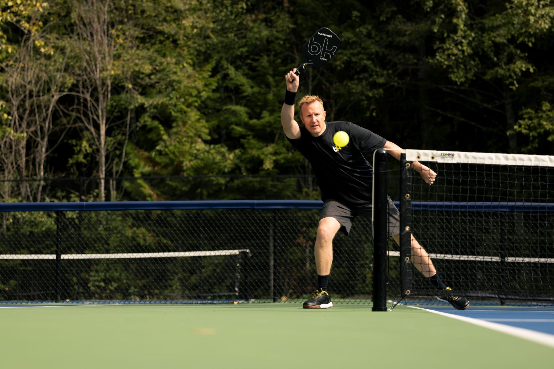 Person playing pickleball on a court with trees in the background