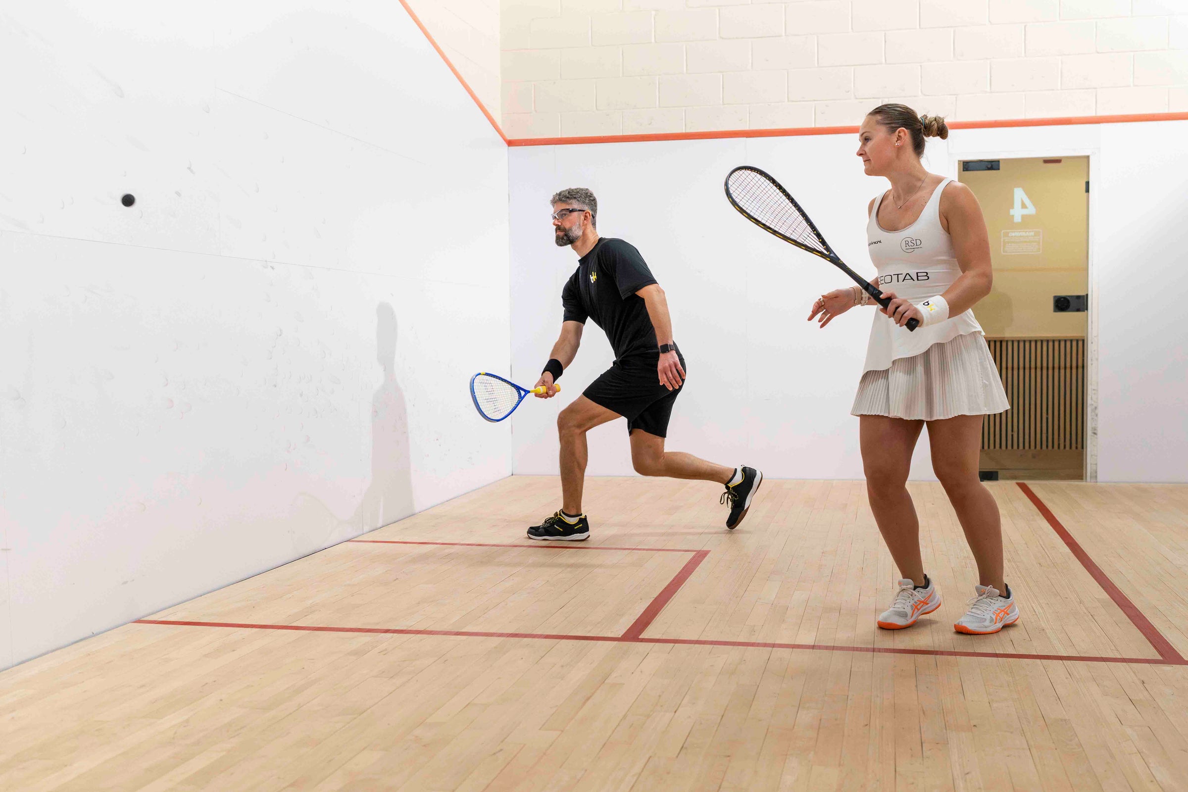 Two people playing squash on a court with racquets.