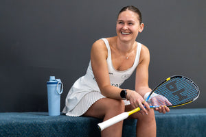 smiling woman sitting on bench holding ProXR squash racquet