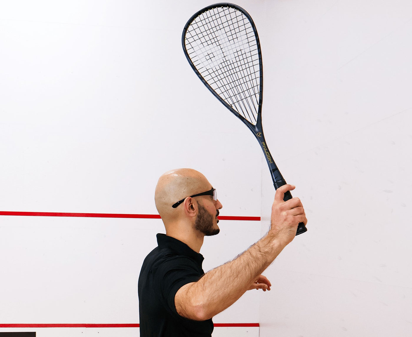 Man holding a squash racket against a white wall with red lines