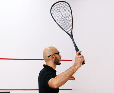 Man holding a squash racket against a white wall with red lines