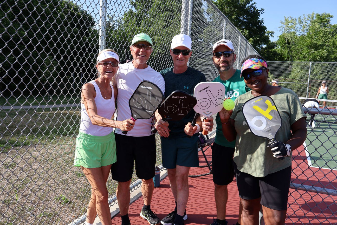 Group of people on a pickleball court holding paddles and balls
